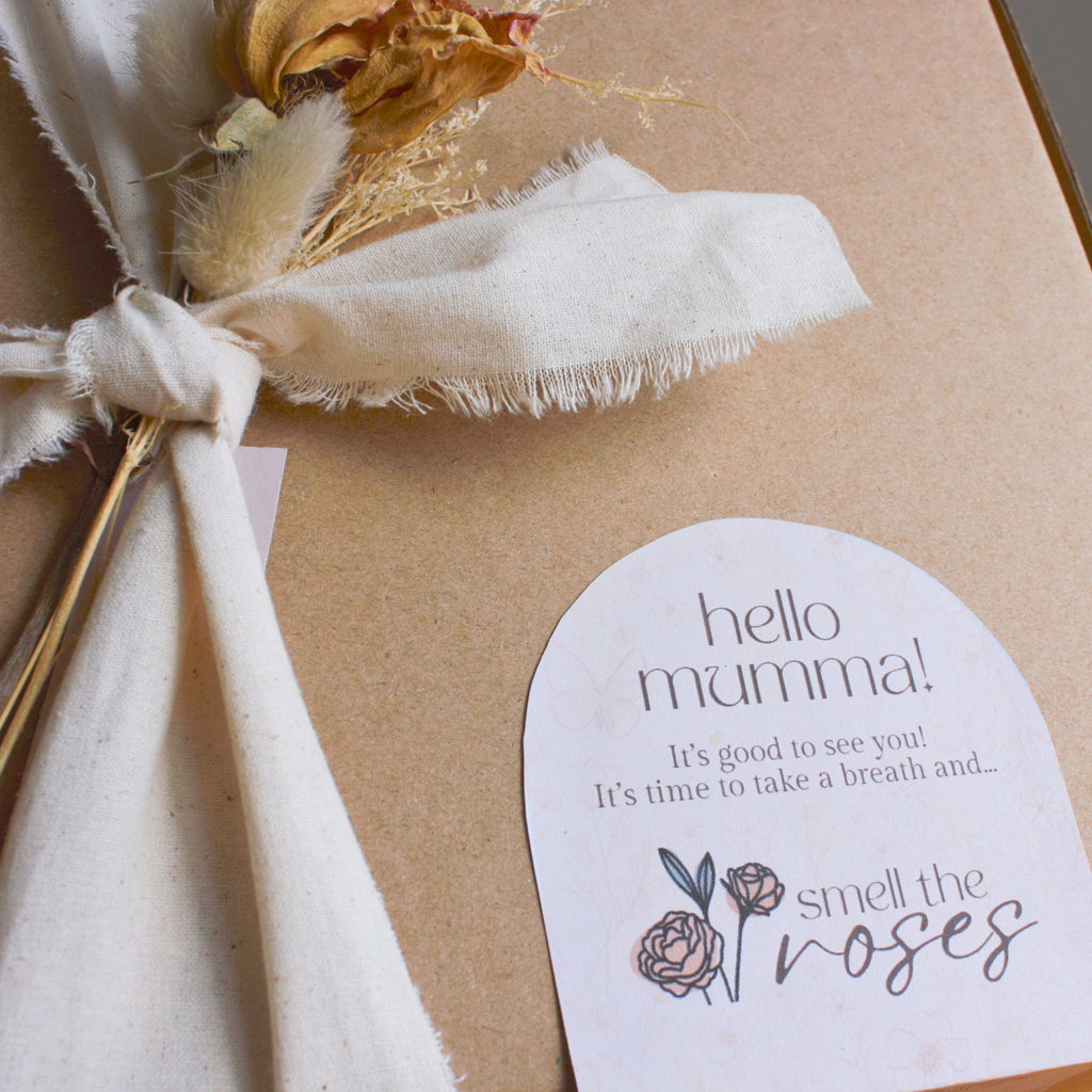Gift with a card that reads 'hello mumma! It's good to see you! It's time to take a breath and smell the roses' on a beige background.