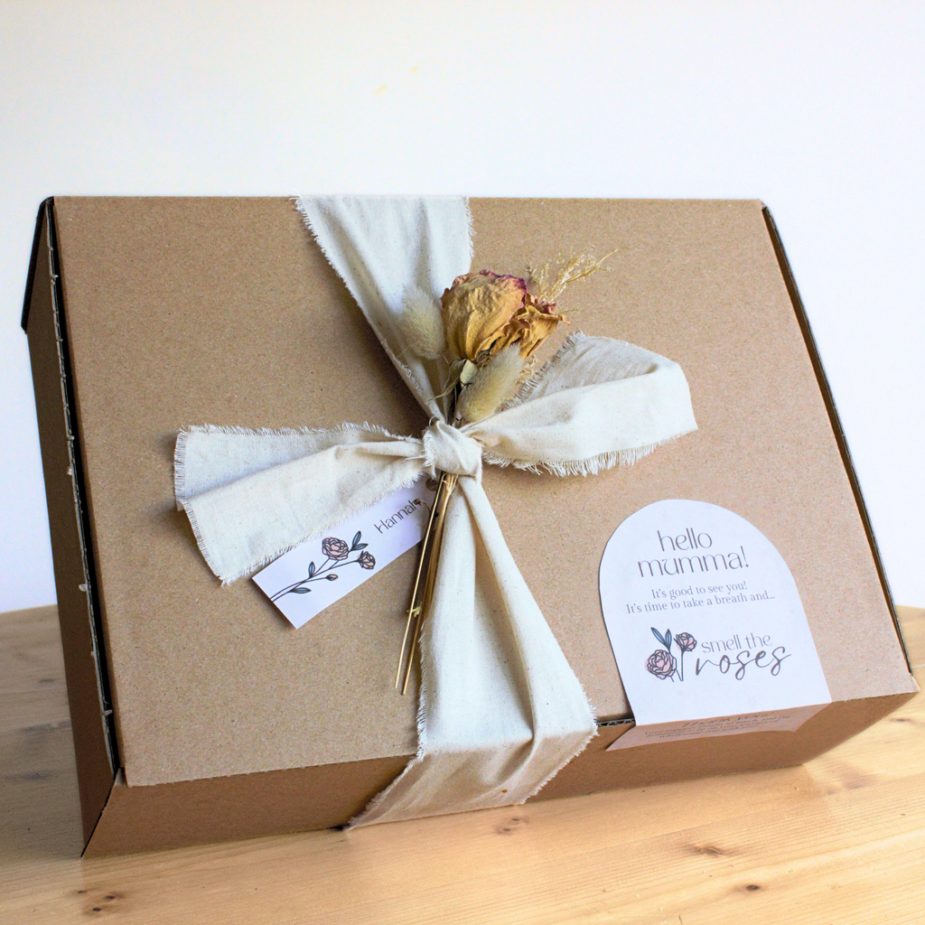 Gift box with a dried flower arrangement and 'hello mum' tag on a wooden surface.