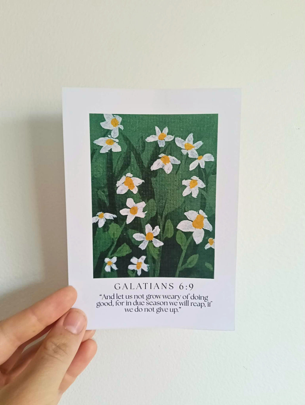 Card with floral design and biblical text held by a hand against a light background